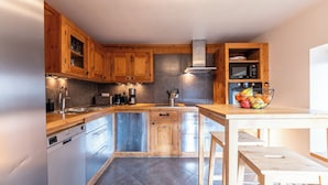 Une cuisine avec des meubles en bois, un évier en acier inoxydable, un lave-vaisselle, un four à micro-ondes et un panier à fruits posé sur le plan de travail.