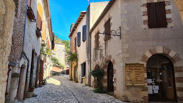 A cobblestone street in a historic town with buildings featuring traditional architecture and a signboard with text.