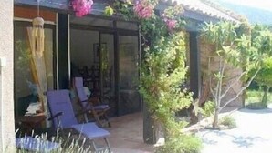 Una casa con un porche cubierto, una puerta de cristal y un pequeño jardín con plantas y flores.