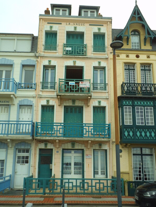 A row of multi-story buildings with balconies, some with green railings and others with blue.