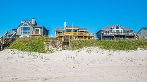 Een pand aan het strand met meerdere huizen, een houten trap naar een terras en een zandstrand op de voorgrond.