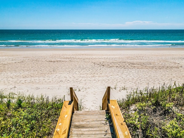 A wooden boardwalk leading to a sandy beach with ocean views.