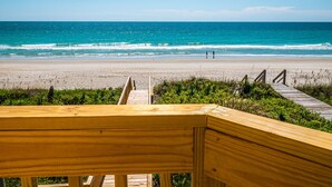 Een houten terras dat uitkomt op een strand, met een helder uitzicht op de oceaan.