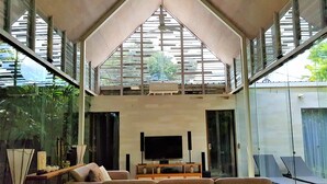 A modern living room with a large sectional sofa, a flat-screen TV, and a glass ceiling allowing natural light.