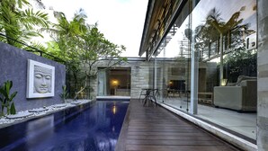 A modern outdoor pool area with a wooden deck, a Buddha statue, and a glass wall leading to a seating area.