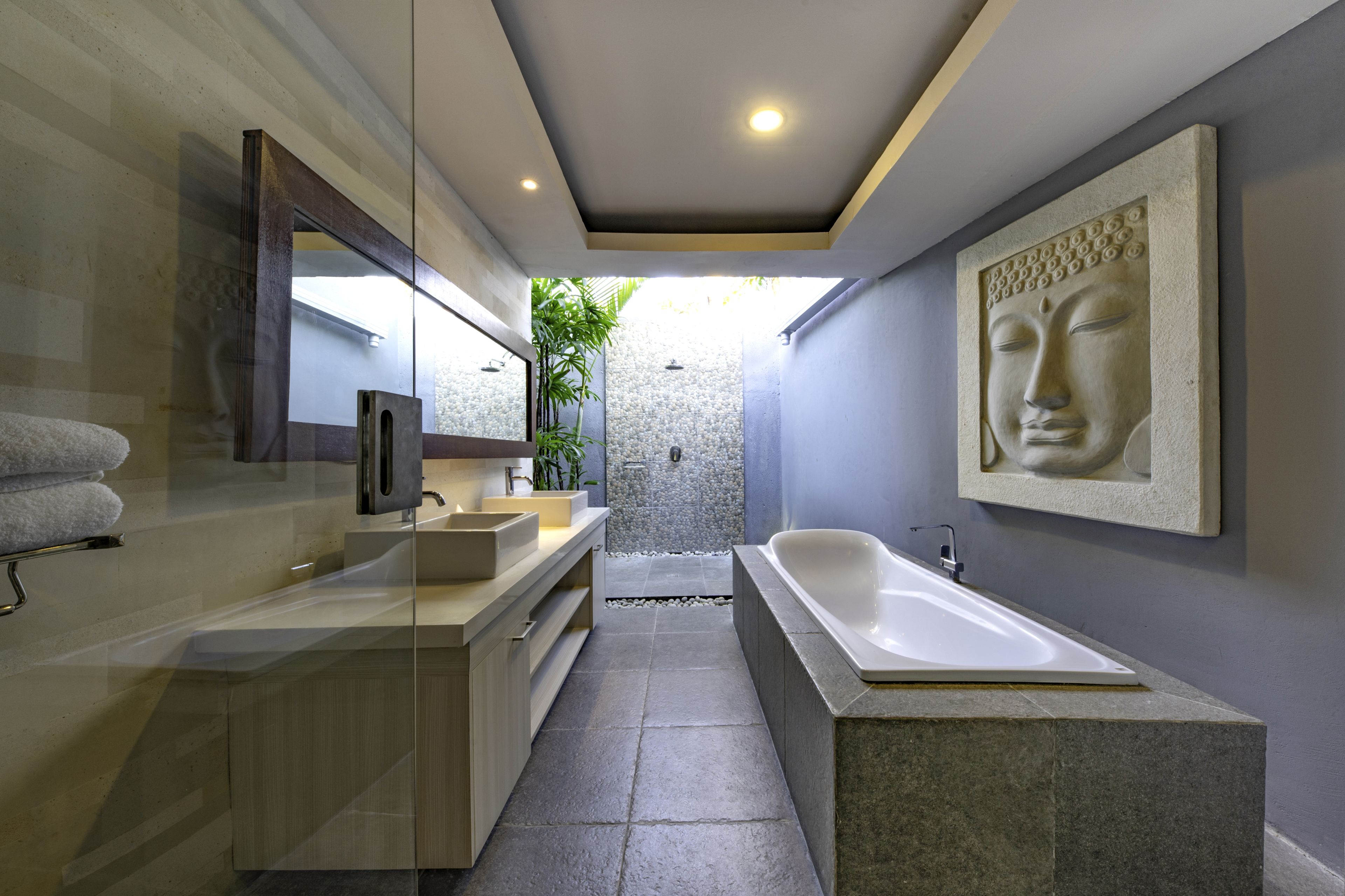 A modern bathroom with a large bathtub, a sink, and a mirror. There is a Buddha statue on the wall and a plant in the corner.