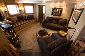 Una sala de estar acogedora con un sofá, una mesita de centro y una mesa pequeña con un tablero de ajedrez. Hay un árbol de Navidad y una chimenea.