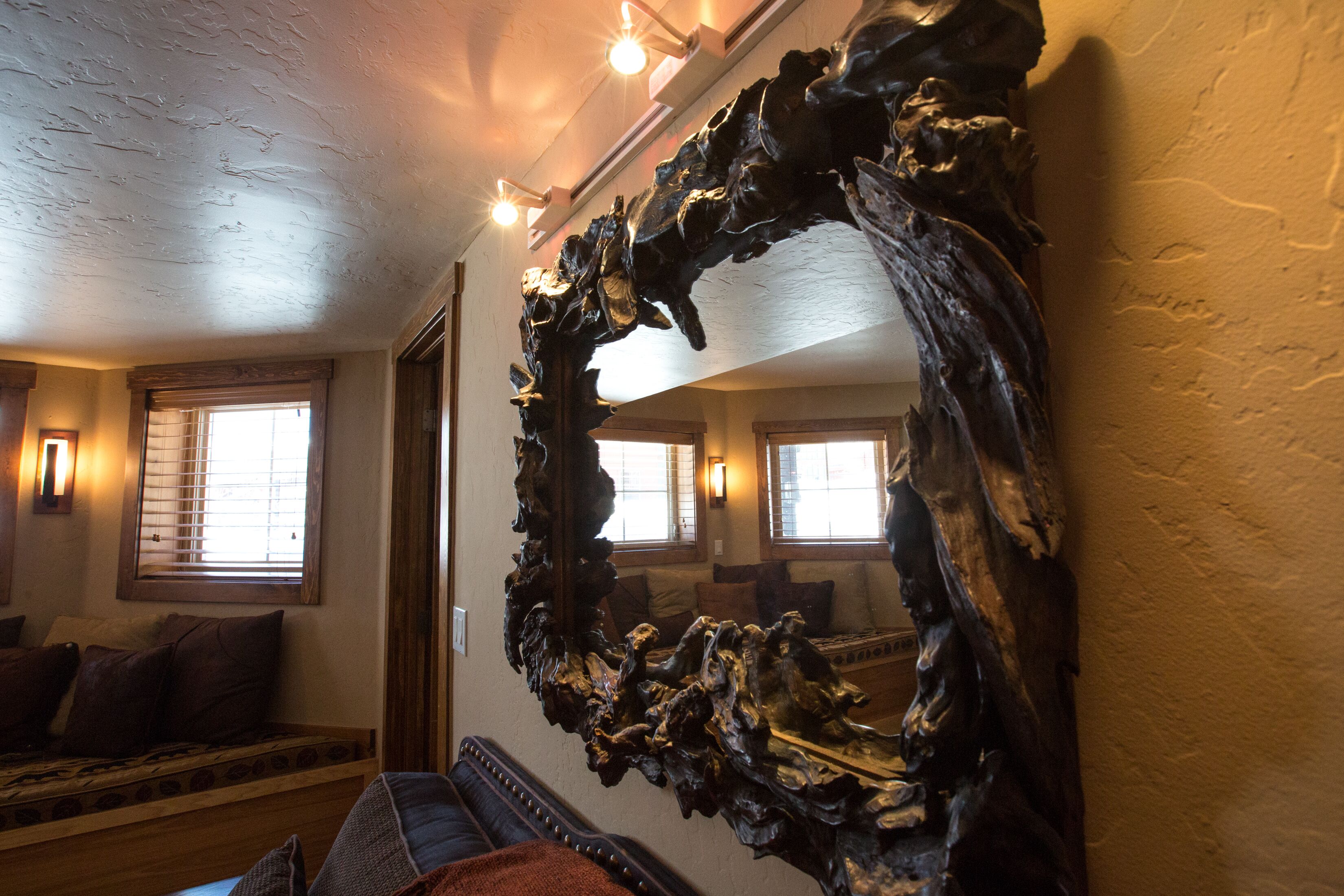 A room with a large, natural wood-framed mirror, a wooden bench, and a window with blinds.