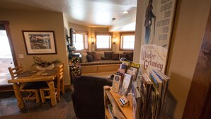 A cozy room with a wooden dining table, a comfortable sofa, and a bookshelf filled with books and magazines. - Luxury Apt,  Private Hot Tub, Couples Retreat (Breckenridge)
