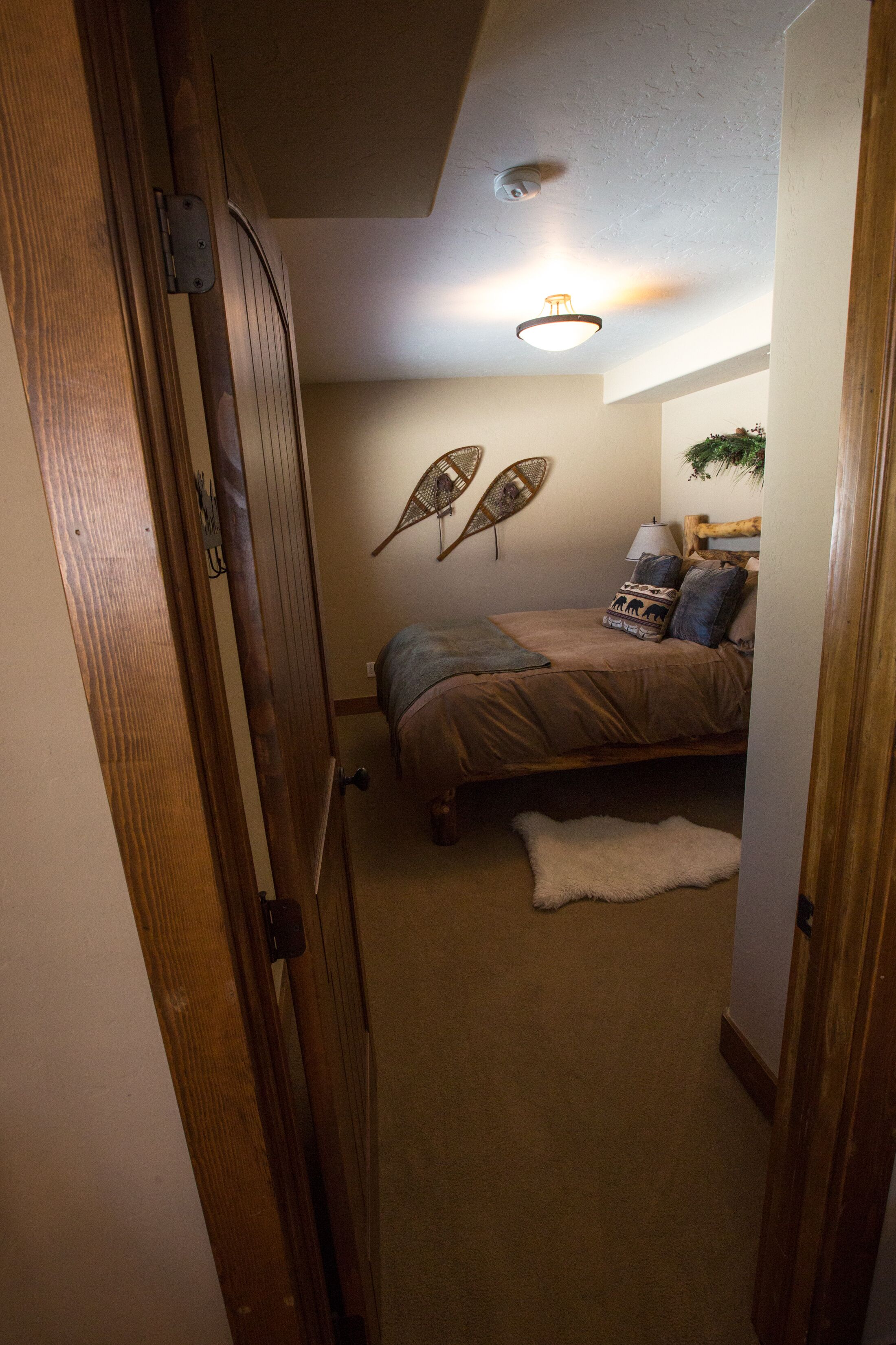 A bedroom with a bed, a bedside lamp, a wall-mounted fan, and a small rug.
