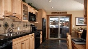 A kitchen with wooden cabinets, a black countertop, and a view of a snowy landscape through a glass door. - Luxury Apt,  Private Hot Tub, Couples Retreat (Breckenridge)