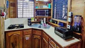 A rustic kitchen with wooden cabinets, a gas stove, a microwave, and a coffee maker. - Baby Blue Cabana (Hopkins Village)