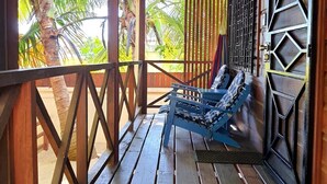 A wooden porch with a bench, a metal gate, and a view of palm trees. - Baby Blue Cabana (Hopkins Village)