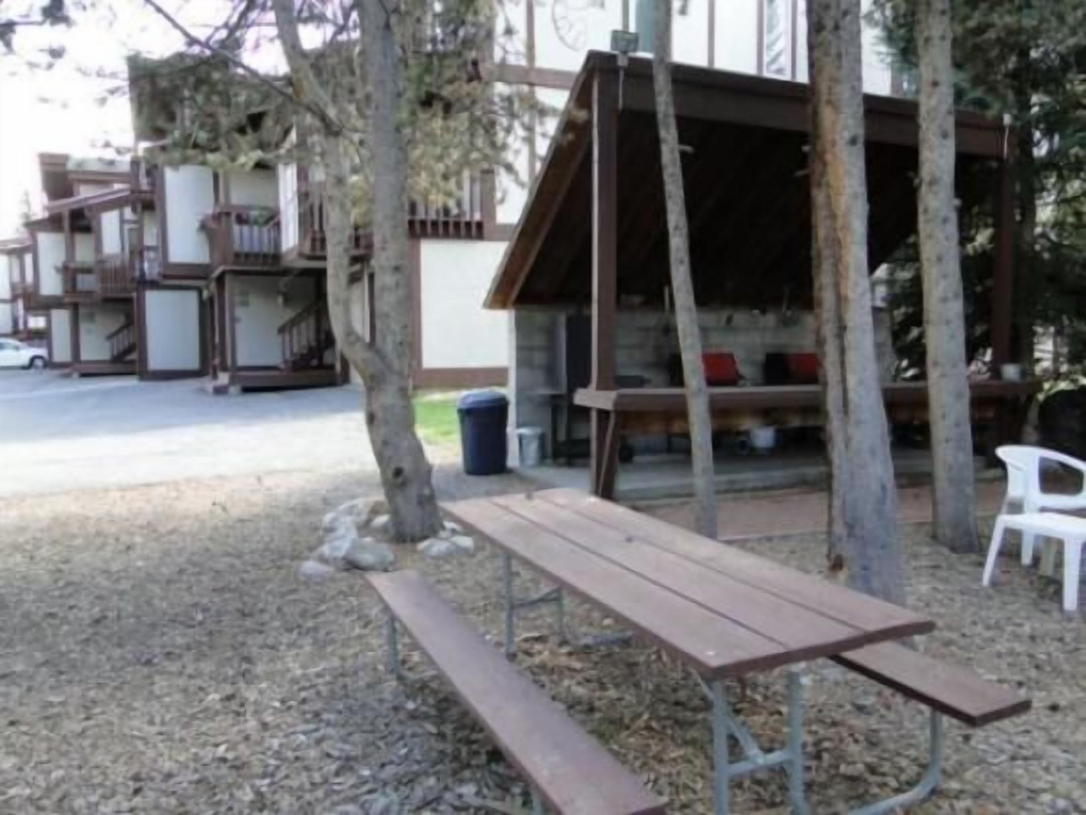 Una mesa de picnic en un parque, con un banco de madera y un pequeño refugio.