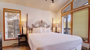 A bedroom with a large bed, two bedside tables with lamps, a window with blinds, and a radiator.