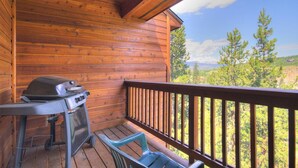 Una terraza de madera con una parrilla y sillas, con vistas a un paisaje boscoso.