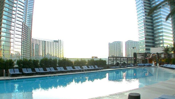 Ein Pool auf dem Dach mit Liegestühlen, umgeben von Hochhäusern.