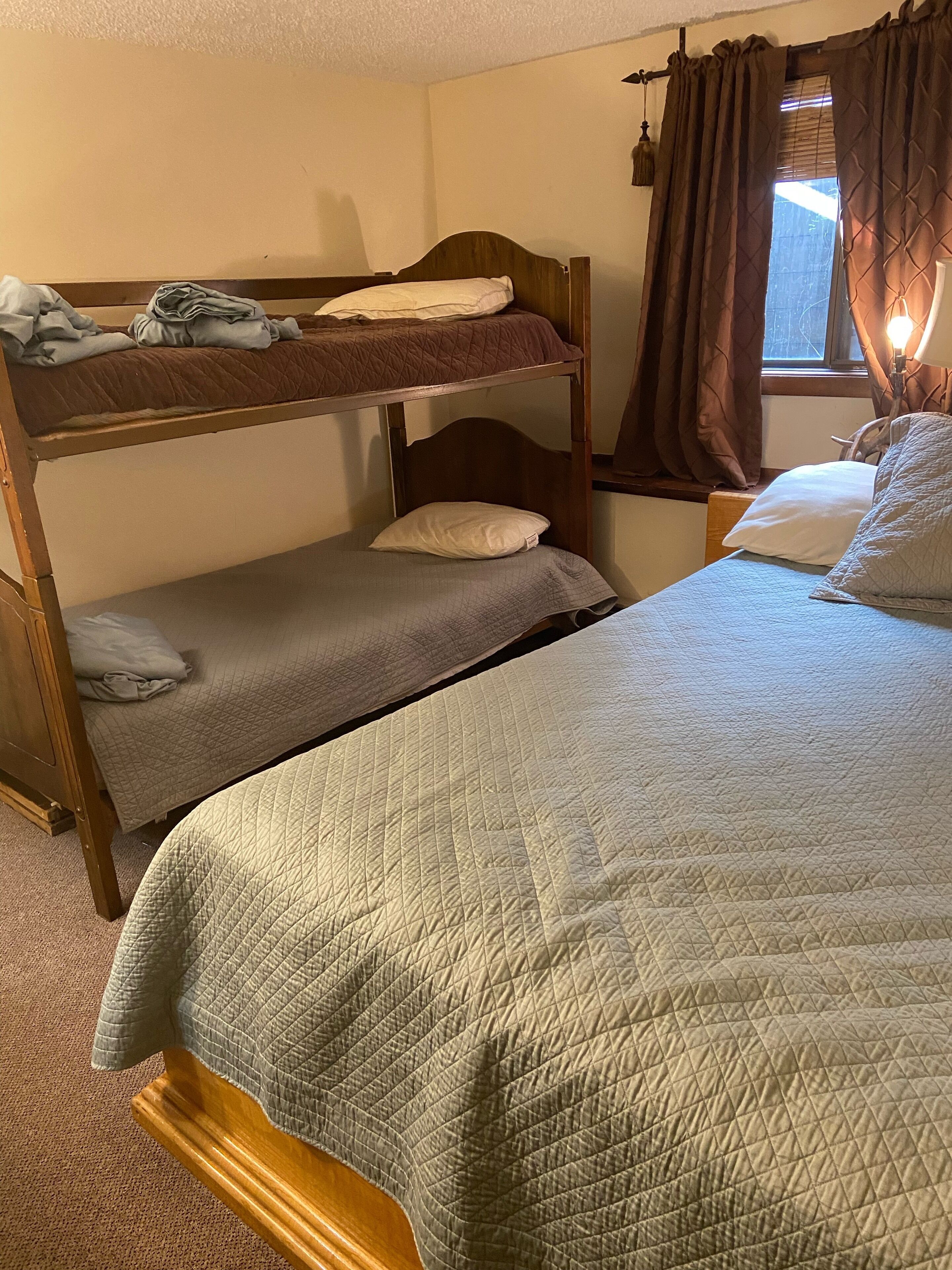 A bunk bed room with two beds, a window with curtains, and a lamp on the nightstand.