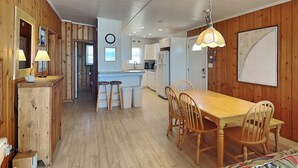 A spacious kitchen with wooden walls, a dining area with a wooden table and chairs, and a kitchen island with stools. - Mamaw's Spot | Oceanfront + Pet Friendly! (Topsail Beach)
