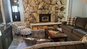 Una sala acogedora con chimenea de piedra, dos sillones estampados, un sofá y una mesita de centro.