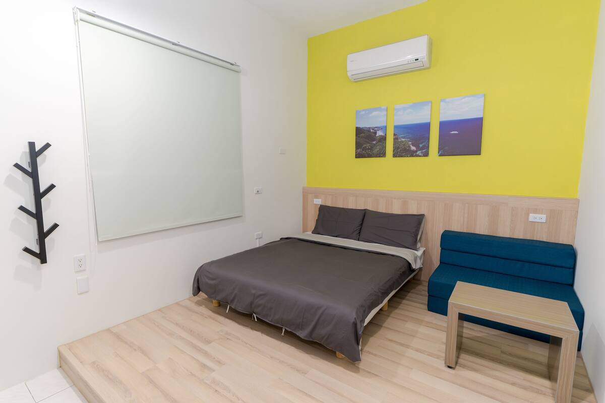 A room with a bed, a blue sofa, a small table, and a whiteboard on the wall.