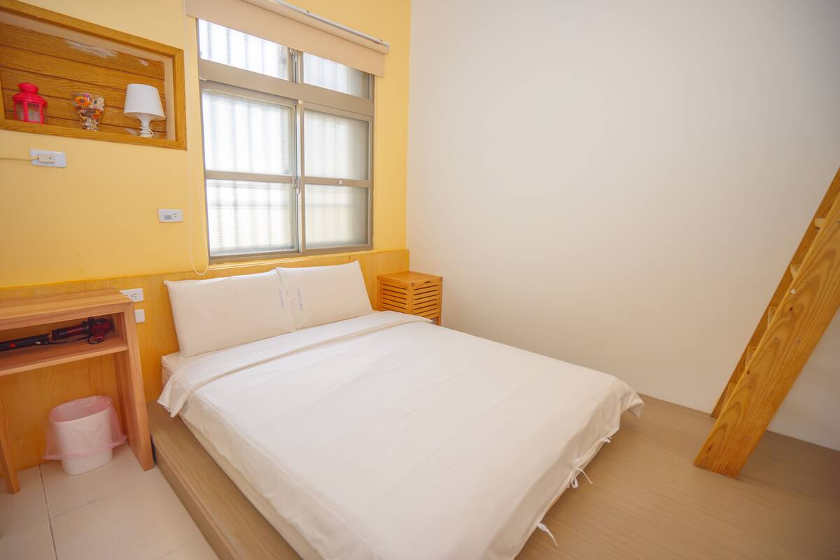 A bedroom with a bed, a desk, and a window.