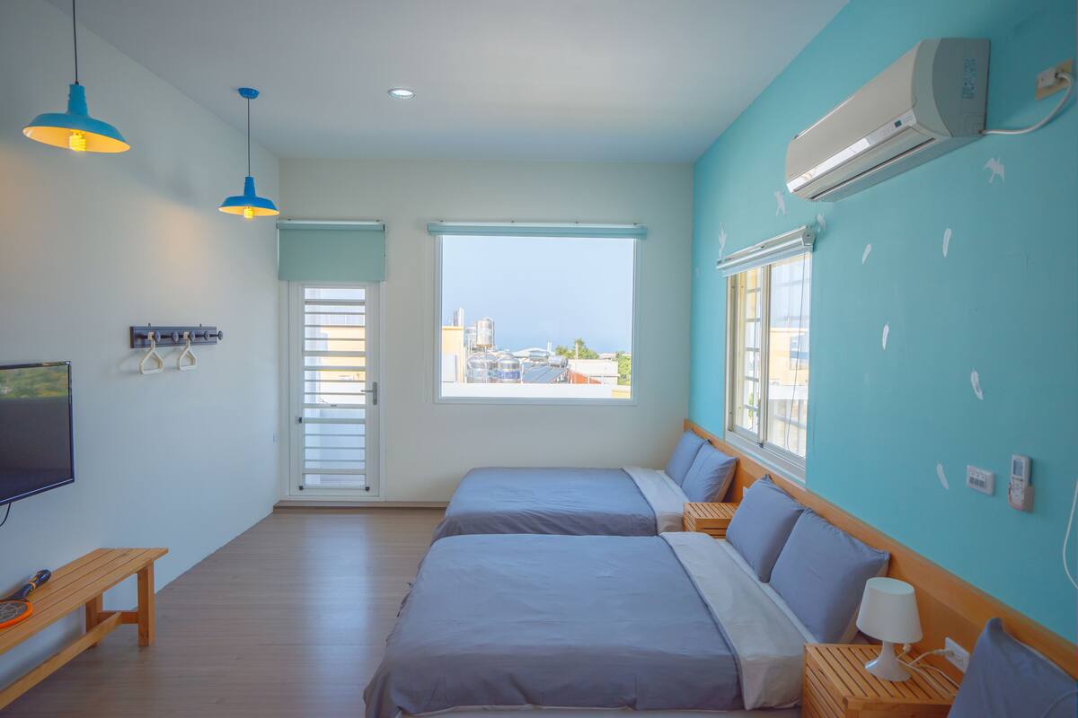A room with two beds, a TV, and a window with a view of the city.