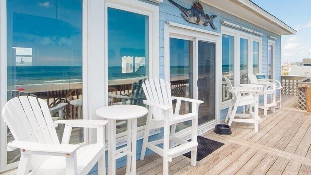 Une terrasse avec des chaises et des tables blanches, d’où l’on a une vue sur l’océan.