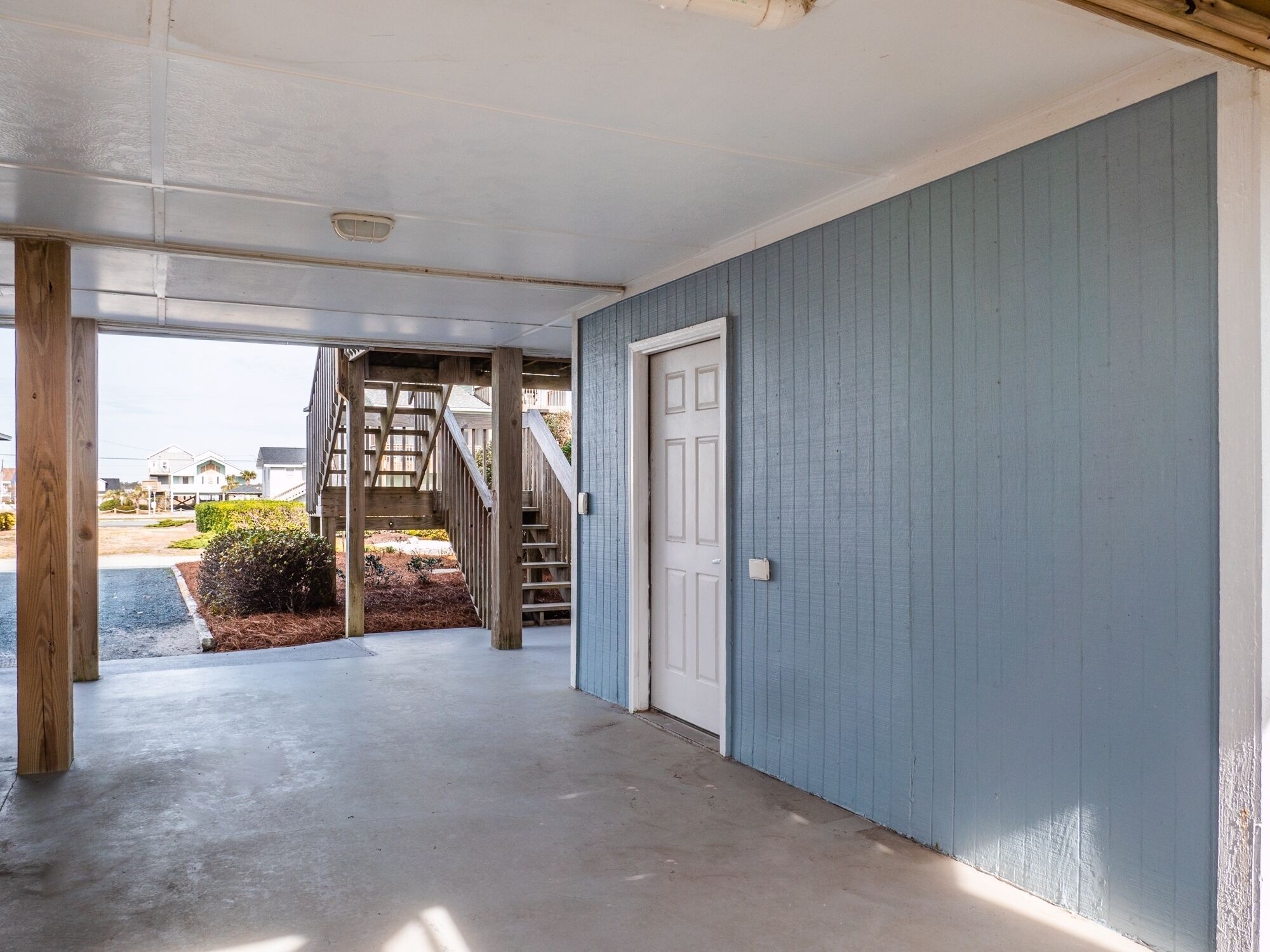 A covered entryway with a concrete floor, a wooden staircase, and a white door.
