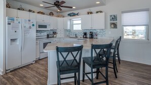 Une cuisine moderne avec des meubles blancs, un îlot central et un ventilateur de plafond.