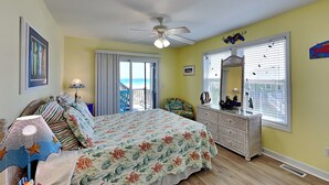 Een slaapkamer met een bed, een dressoir en uitzicht op de oceaan door een schuifdeur.