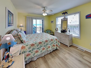 A bedroom with a bed, dresser, and a view of the beach through the window.