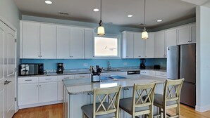 Una cucina moderna con mobili bianchi, un'isola centrale con sgabelli da bar, un frigorifero in acciaio inossidabile e luci a sospensione.