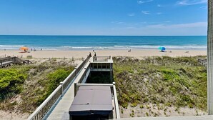 Vista sulla spiaggia con una passerella di legno che conduce a un edificio con tetto piatto.