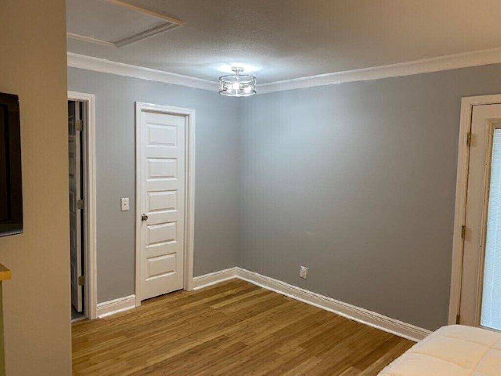 A room with a wooden floor, a white door, and a ceiling light fixture.