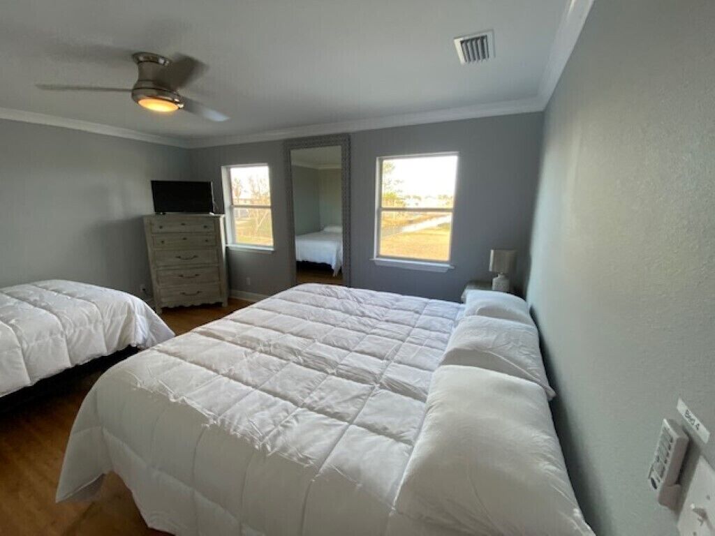 Een slaapkamer met twee bedden, een kaptafel, een plafondventilator en een groot raam.