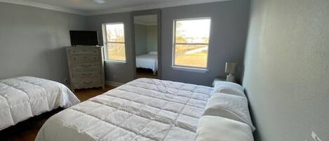 Een slaapkamer met twee bedden, een kaptafel, een plafondventilator en een groot raam.