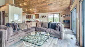 A spacious living room with a large sectional sofa, a glass coffee table, and a wooden ceiling. - Spectacular 180° Beaver Lakefront Views! Steps to Shoreline+Pool Table+Fire Pit (Garfield)