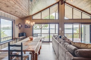 A spacious room with a wooden ceiling, large windows, a dining table, a sofa, and a view of a lake. - Spectacular 180° Beaver Lakefront Views! Steps to Shoreline+Pool Table+Fire Pit (Garfield)