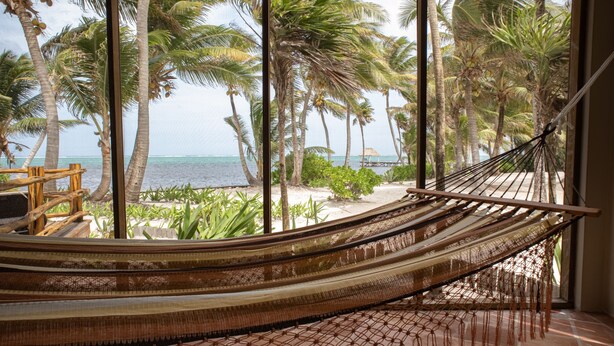 Eine Hängematte in einem Zimmer mit Blick auf einen Strand und Palmen.