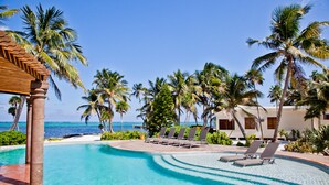 Ein Poolbereich mit Liegestühlen und Palmen, mit Blick auf das Meer.