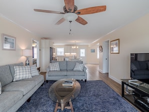 A spacious living room with a grey sofa, a coffee table, and a ceiling fan. - Bear's Den | Canal Front + Boat Dock! (Topsail Beach)