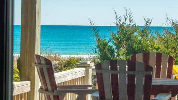 Una terraza de madera con sillas Adirondack con vista a una playa y al océano.