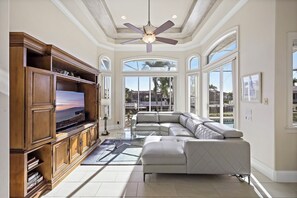 A spacious living room with a large sectional sofa, a wooden entertainment unit, and a ceiling fan.
