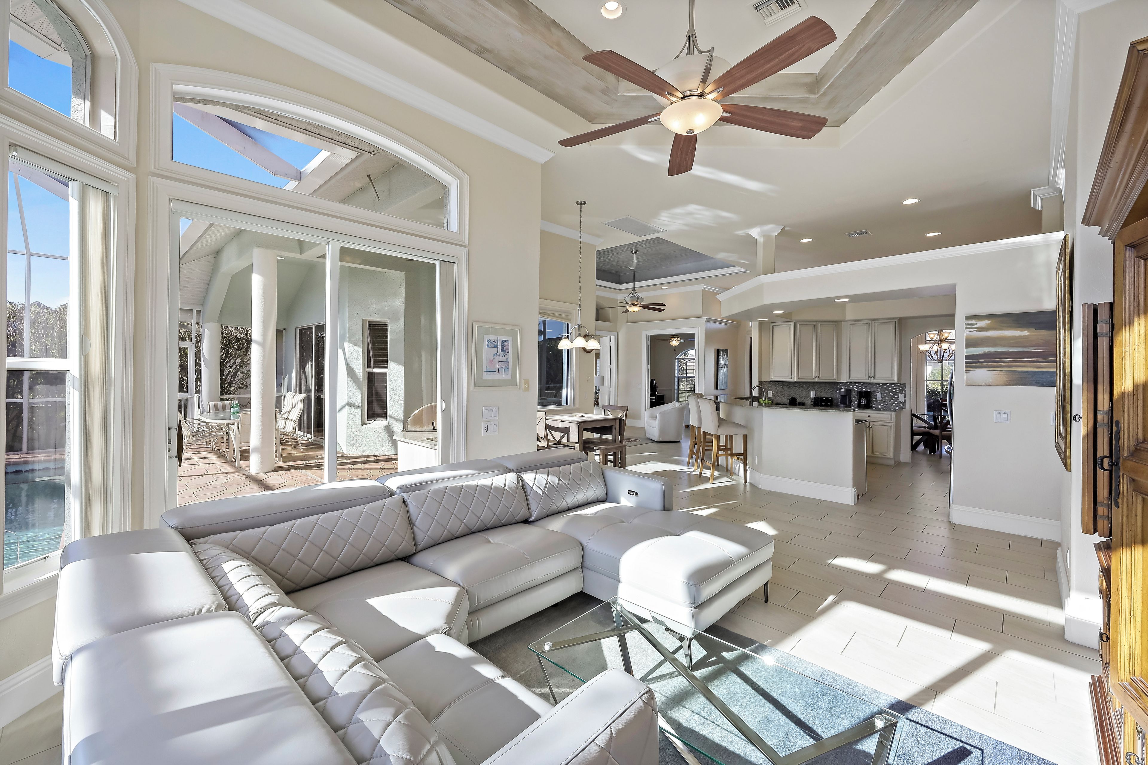 A spacious living area with a large sectional sofa, a glass coffee table, and a ceiling fan.