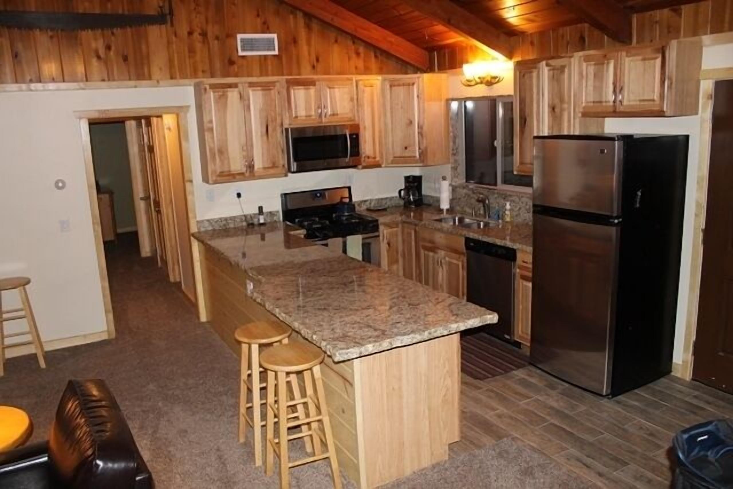 A kitchen with wooden cabinets, a granite countertop, a stainless steel refrigerator, and a built-in stove.