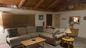 A cozy living room with a sectional sofa, a wooden coffee table, and a small side table with a lamp. - Walking distance to Snow Summit! (Big Bear Lake)