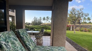 A covered outdoor seating area with a pool table and chairs, overlooking a well-maintained garden with palm trees and a stone wall. -  The Shores, quiet, upgraded condo, large lanai w/ garden area and lawn  (Waikoloa)