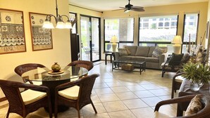 A spacious living area with a glass dining table, wicker chairs, a sofa, and a ceiling fan. -  The Shores, quiet, upgraded condo, large lanai w/ garden area and lawn  (Waikoloa)
