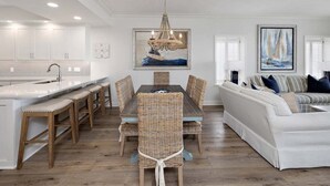 A modern kitchen with white cabinets, a dining area with wicker chairs, and a white sofa in a living room. - Luxurious Oceanfront Condominium (St Simons Island)
